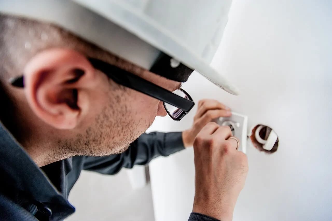 Elektrikář v helmě montuje zásuvku na zdi